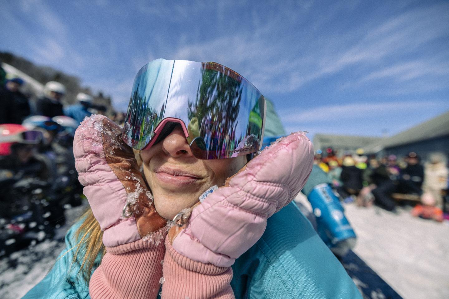 Sourire dans la neige, lunettes réfléchissantes, gants roses, journée ensoleillée.