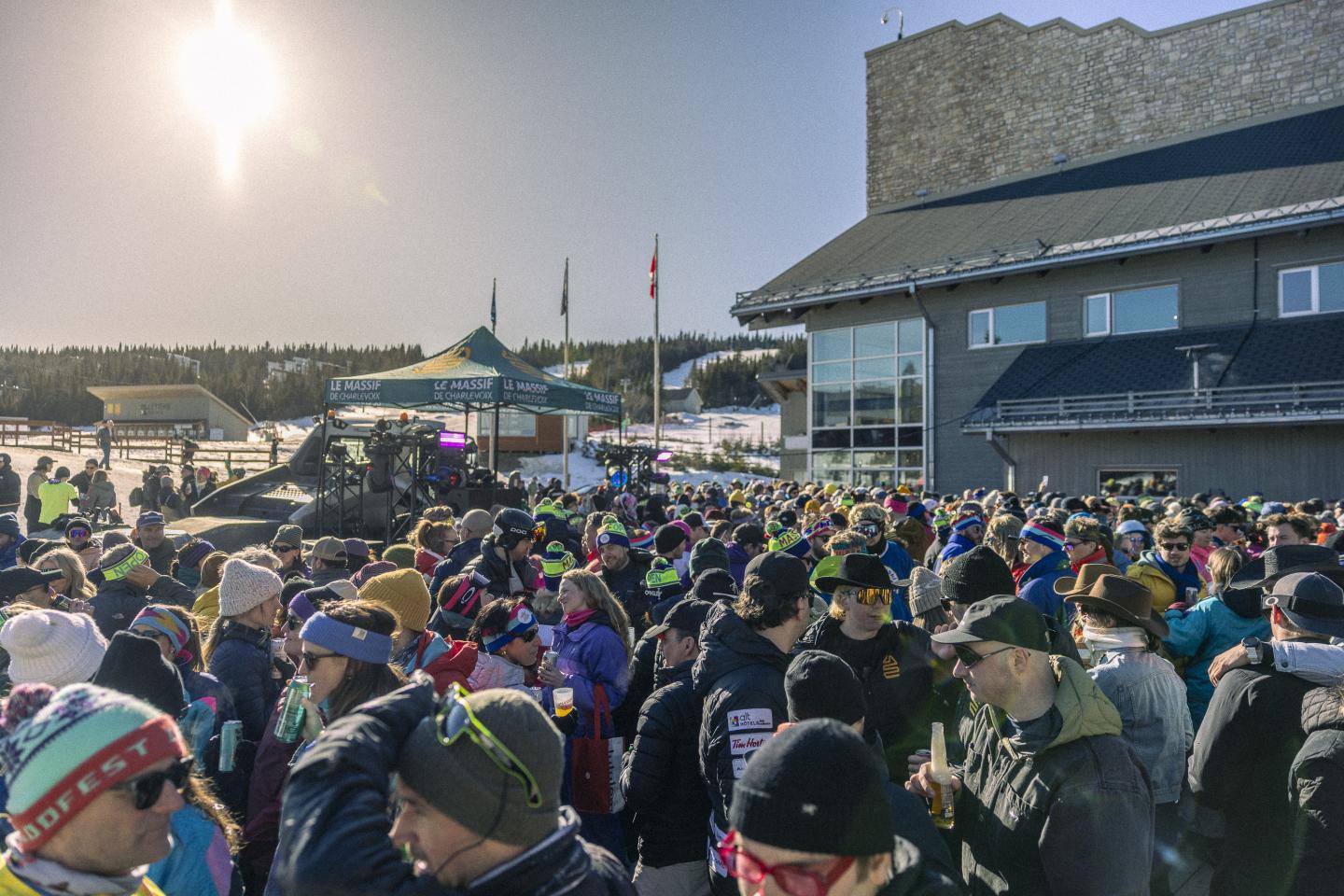Foule de personnes en plein air sous le soleil, près d'un grand bâtiment.