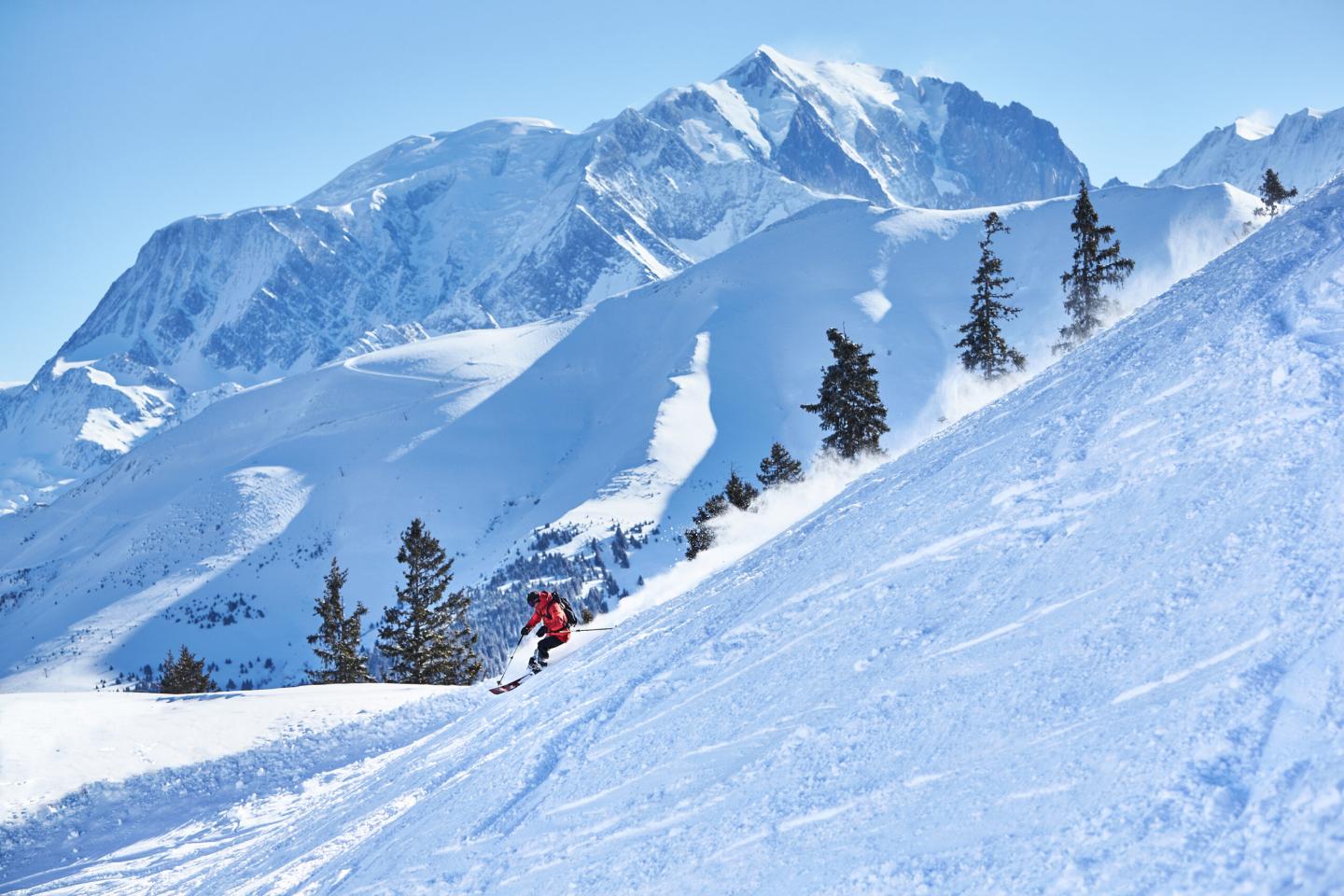 Skieur en descente sur une pente enneigée, montagnes en arrière-plan.