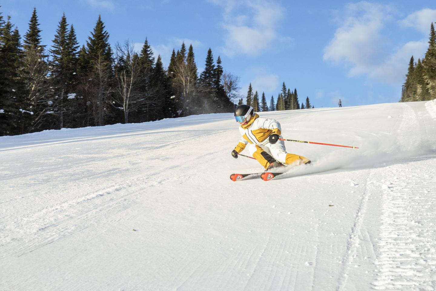 Skieur descendant une piste enneigée sous un ciel bleu.