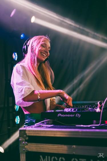 DJ souriante mixant sur scène, éclairée par des lumières colorées.