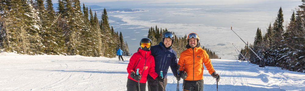Groupe de skieurs souriants sur une piste enneigée, entourés de sapins.