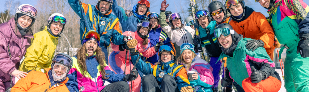Groupe souriant en vêtements de ski colorés sur la neige, ciel bleu en arrière-plan