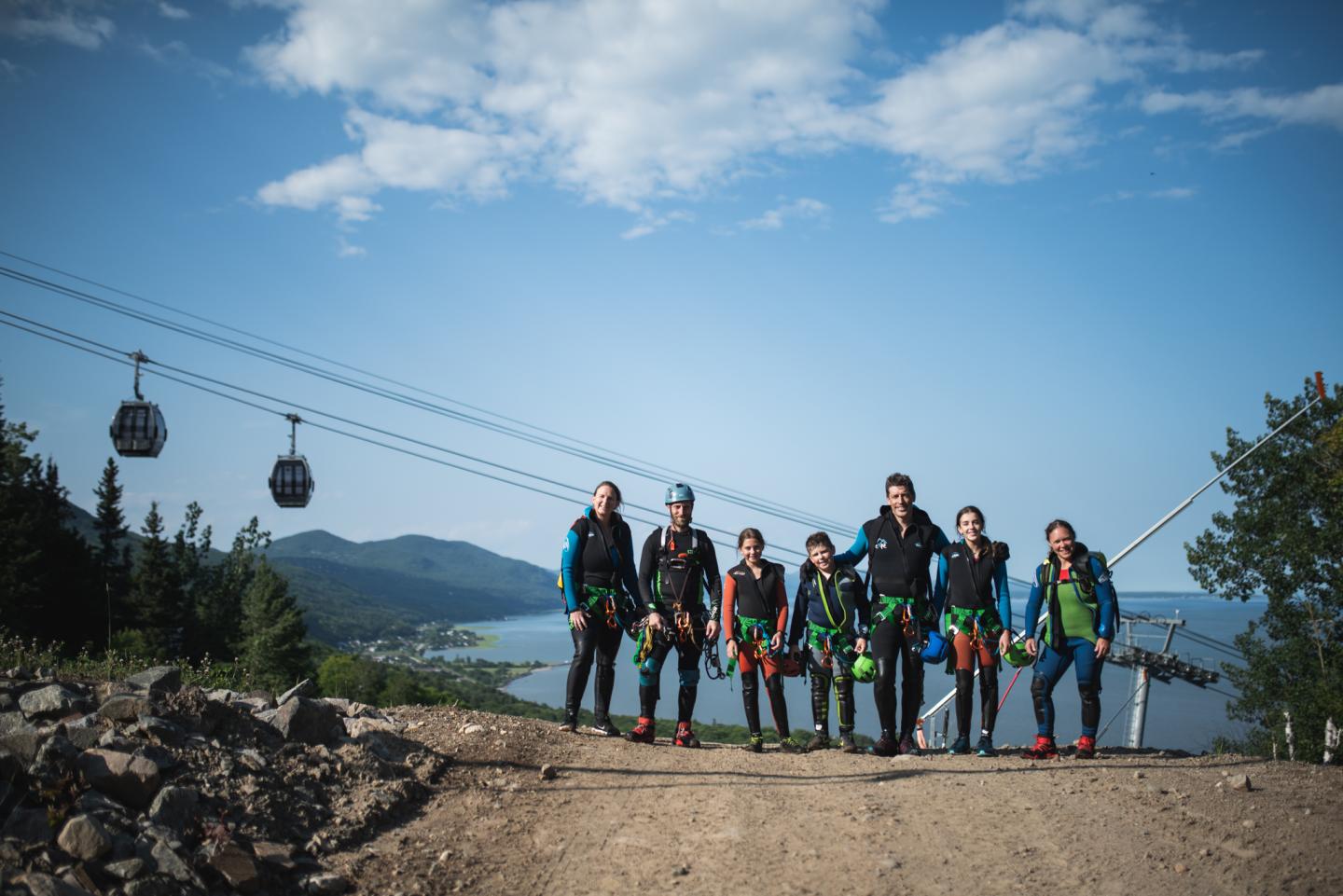 Groupe de personnes en tenue d'escalade sur un chemin avec télécabines en arrière-plan.