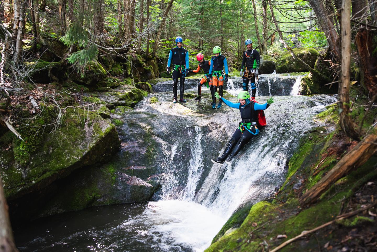 Groupe en combinaison de canyoning, descendant une petite cascade en forêt.