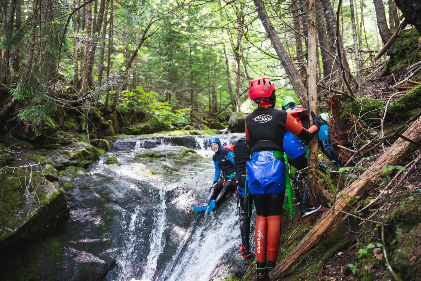 Canyoning dans une forêt, personne en casque rouge près d'une cascade.