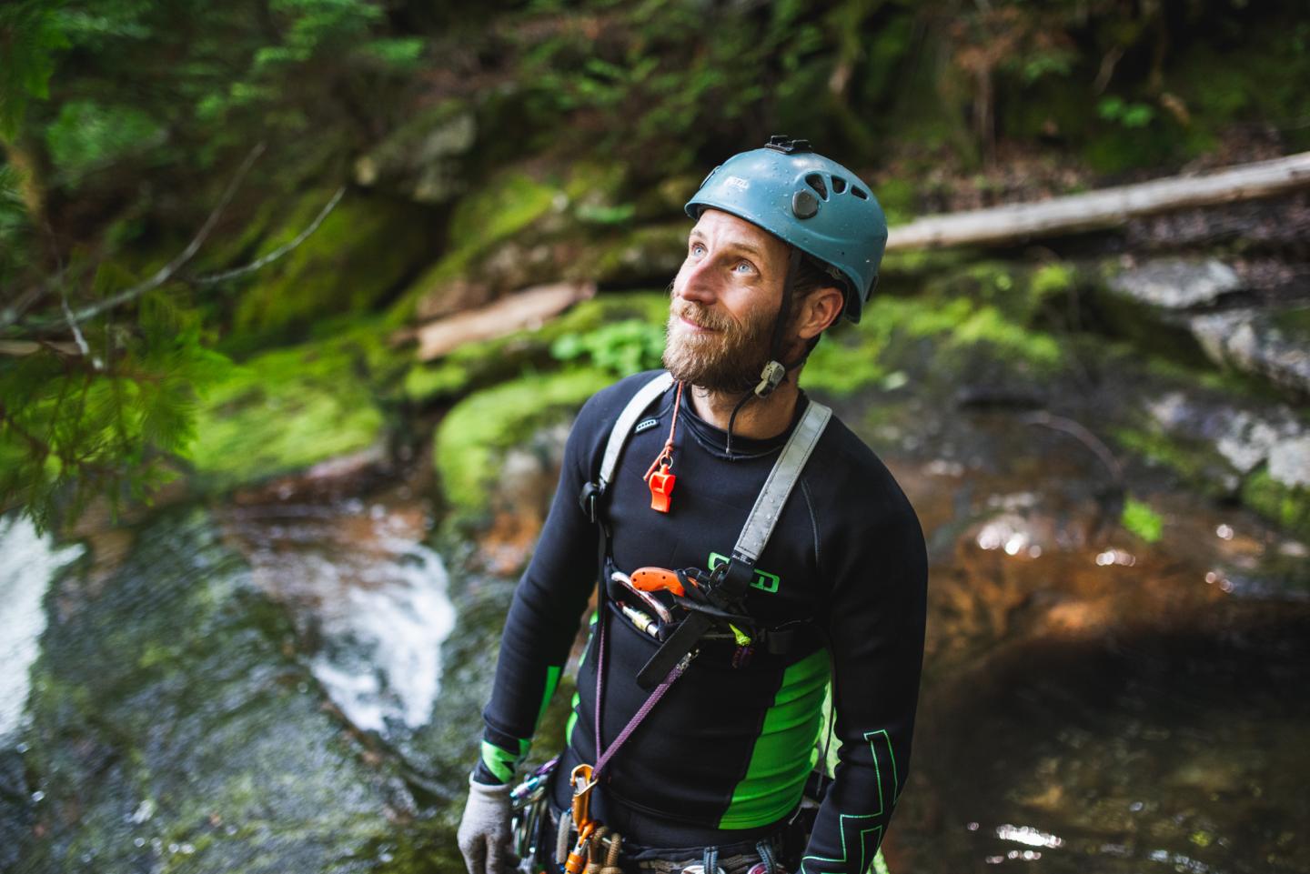 Homme en équipement d'escalade, regardant vers le haut dans une forêt luxuriante.