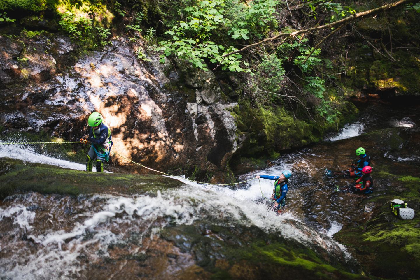 Personnes en tenue de canyoning traversant une rivière en forêt verdoyante.
