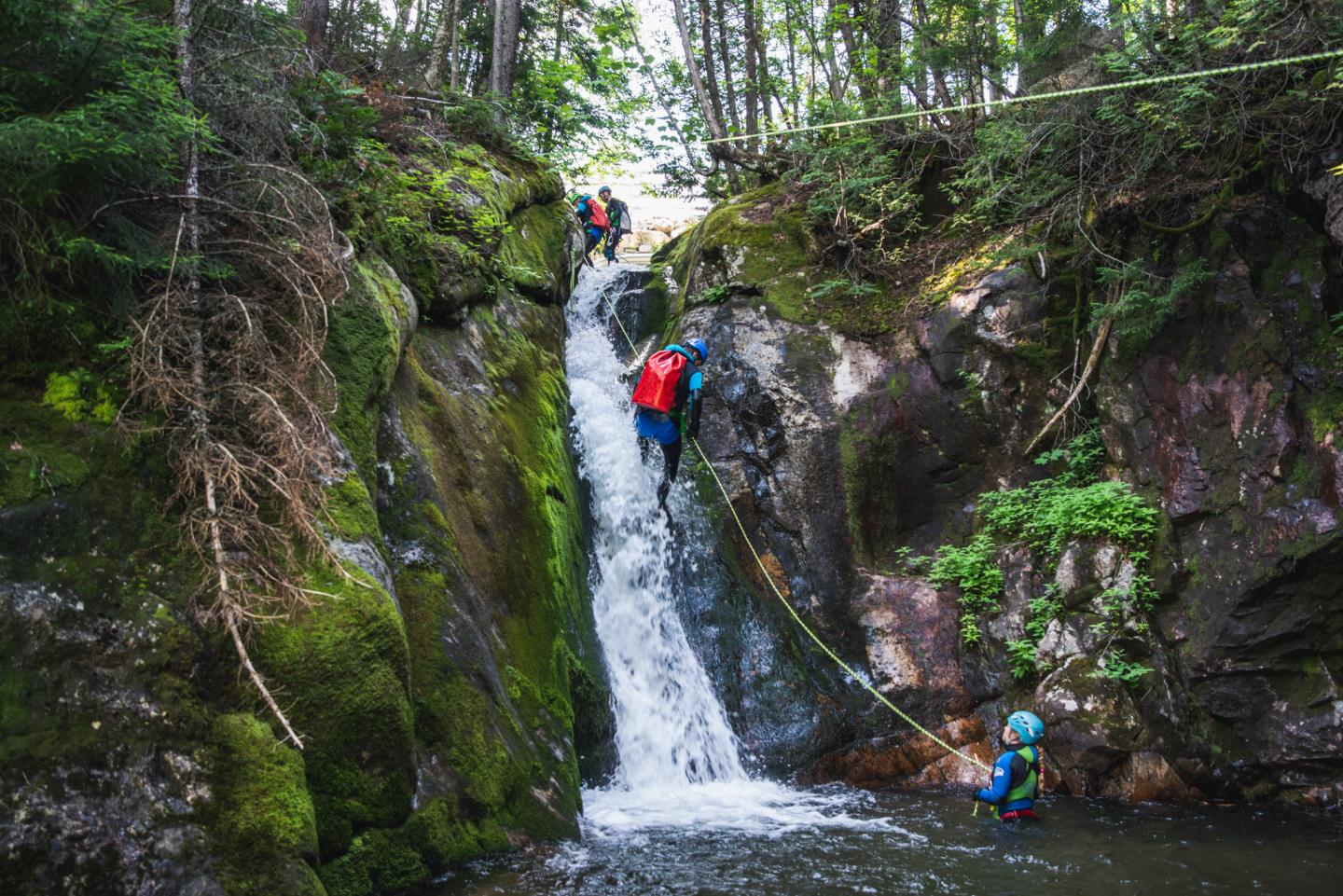 Personnes en canoë devant une cascade dans une forêt verdoyante.