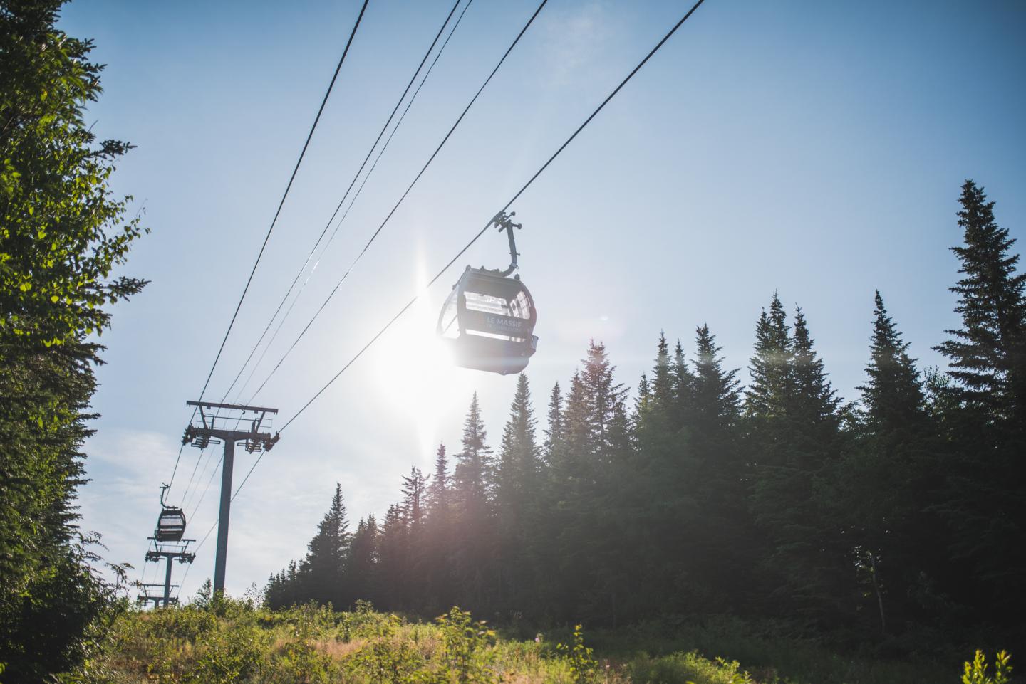 Téléphérique traversant une forêt sous un ciel ensoleillé.