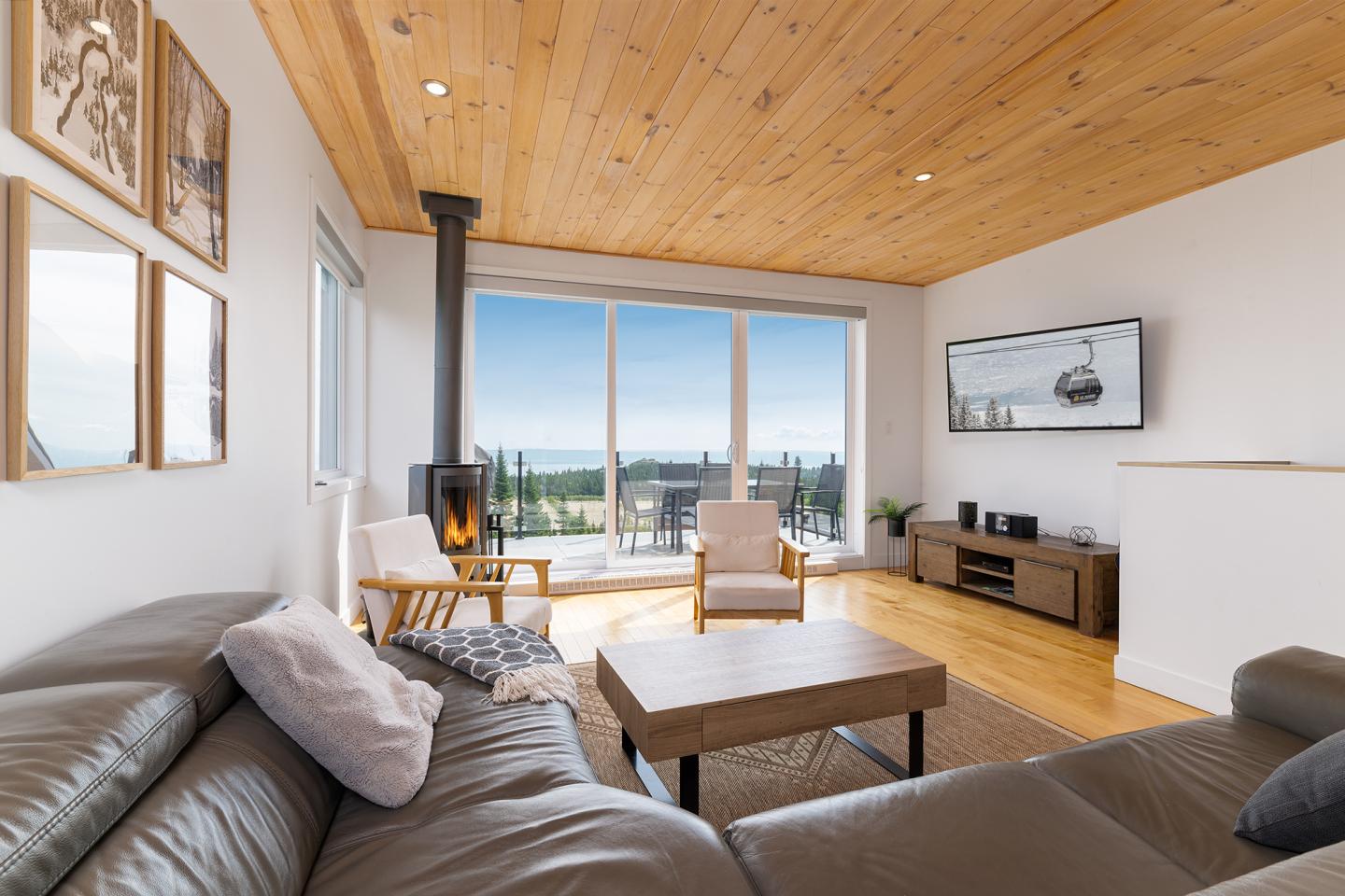 Salon moderne avec plafond en bois, grande baie vitrée et canapé gris.