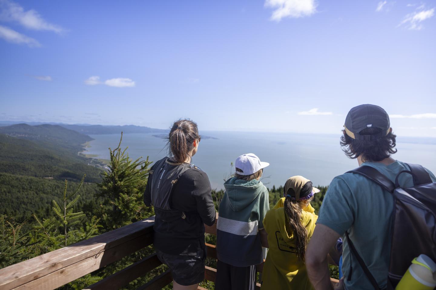Quatre personnes regardent une vue panoramique sur la mer et le littoral, sous un ciel bleu.