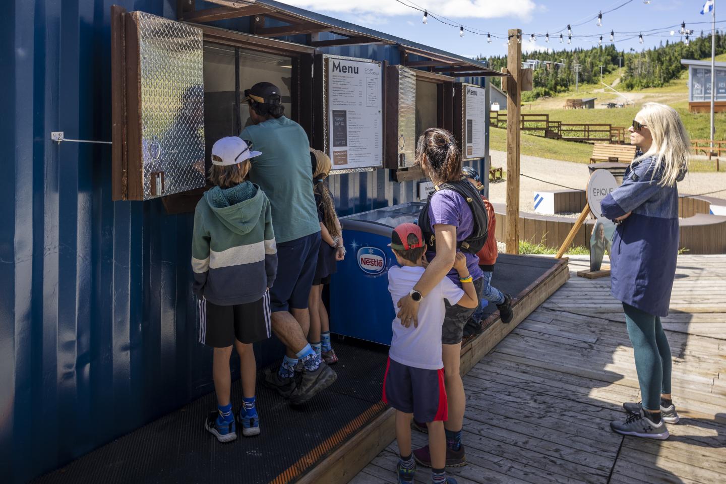 Famille faisant la queue à un stand en plein air par temps ensoleillé.