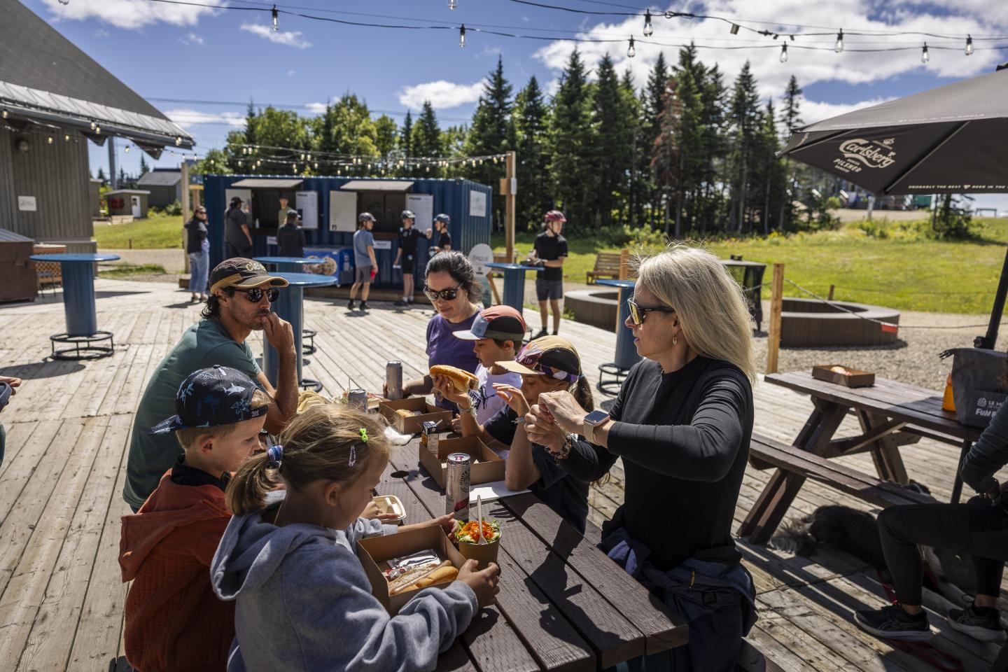 Groupe de personnes autour d'une table en bois à l'extérieur, sous un ciel bleu.