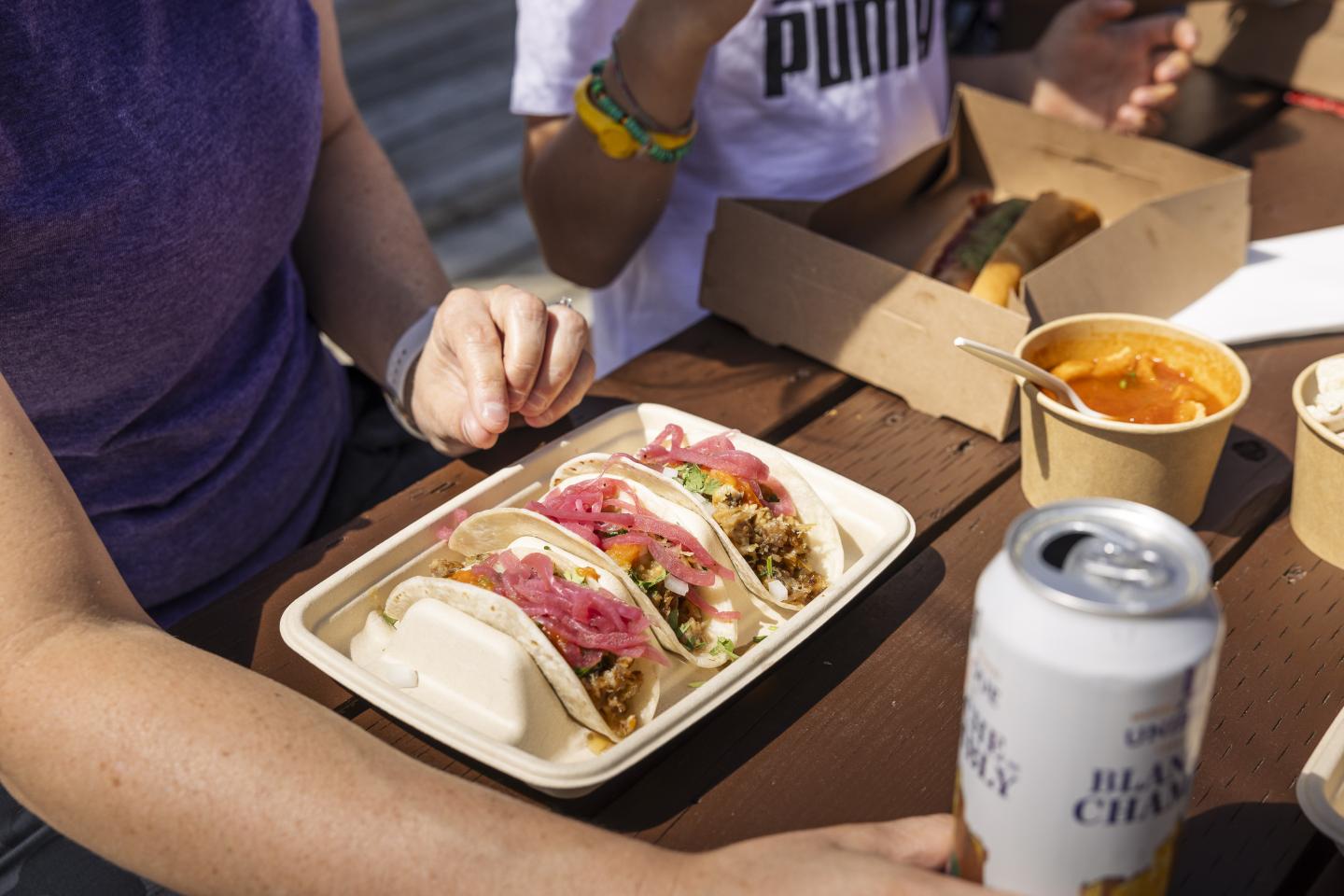 Tacos et bière sur une table en bois, main prête à manger.