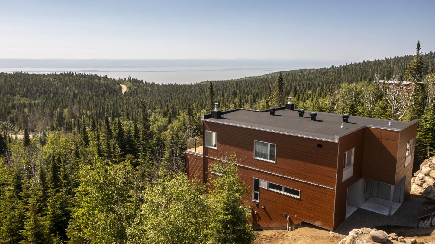 Maison moderne dans la forêt, vue sur la mer en arrière-plan.