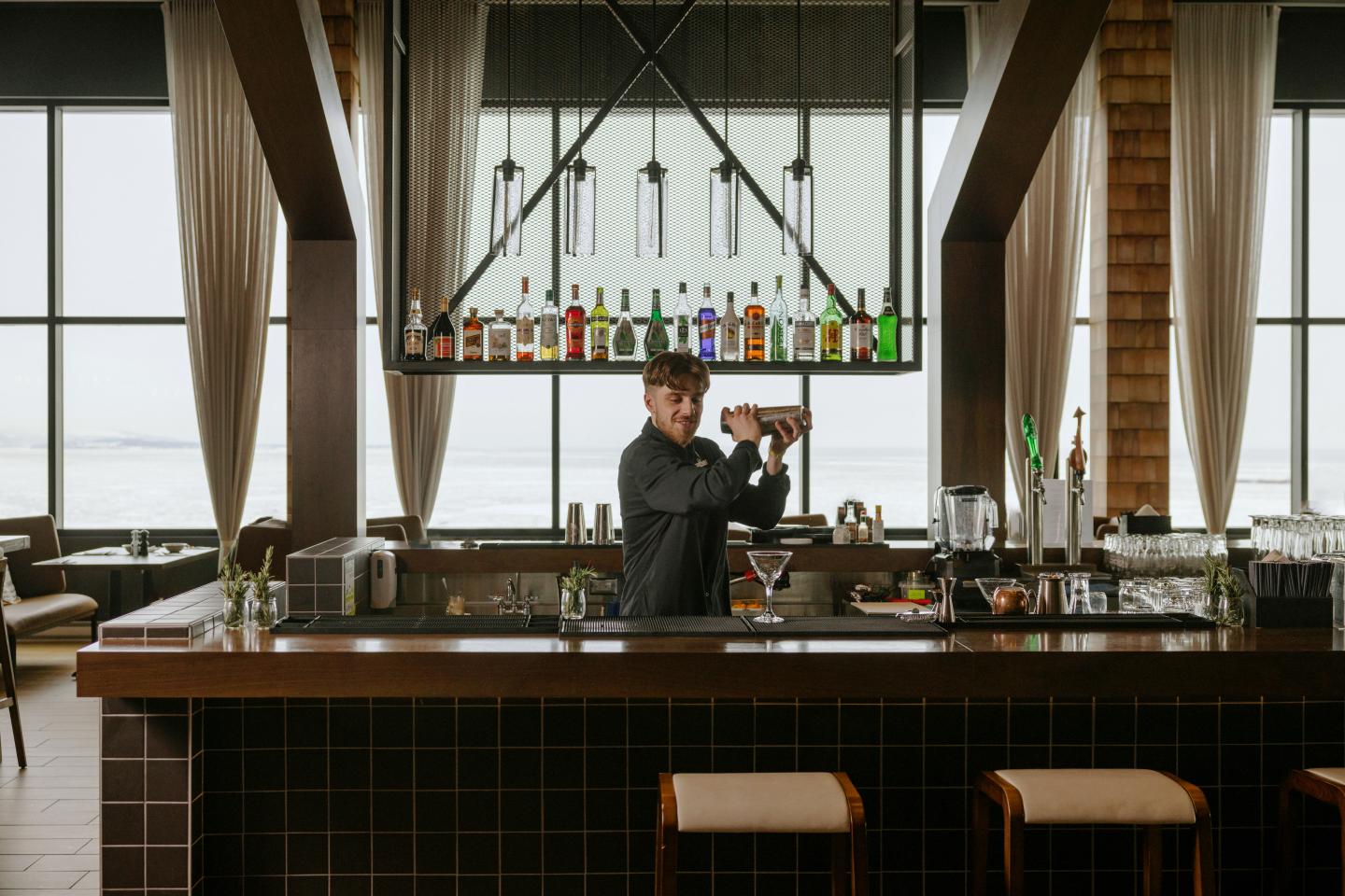Un barman préparant un cocktail dans un bar élégant, bouteilles colorées en arrière-plan.