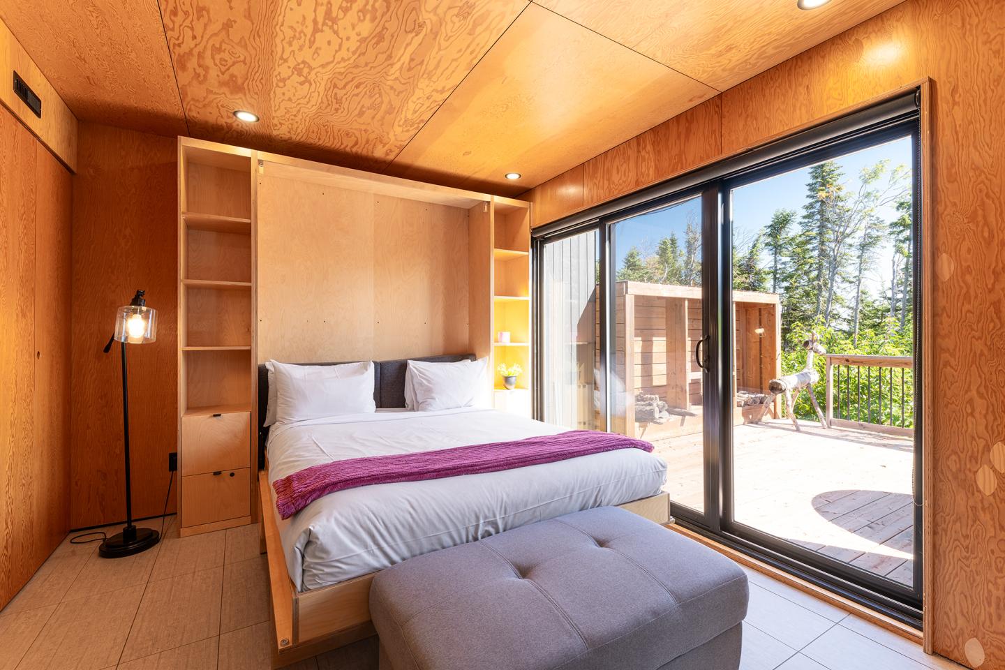 Chambre moderne en bois avec lit double, grande baie vitrée donnant sur une terrasse.