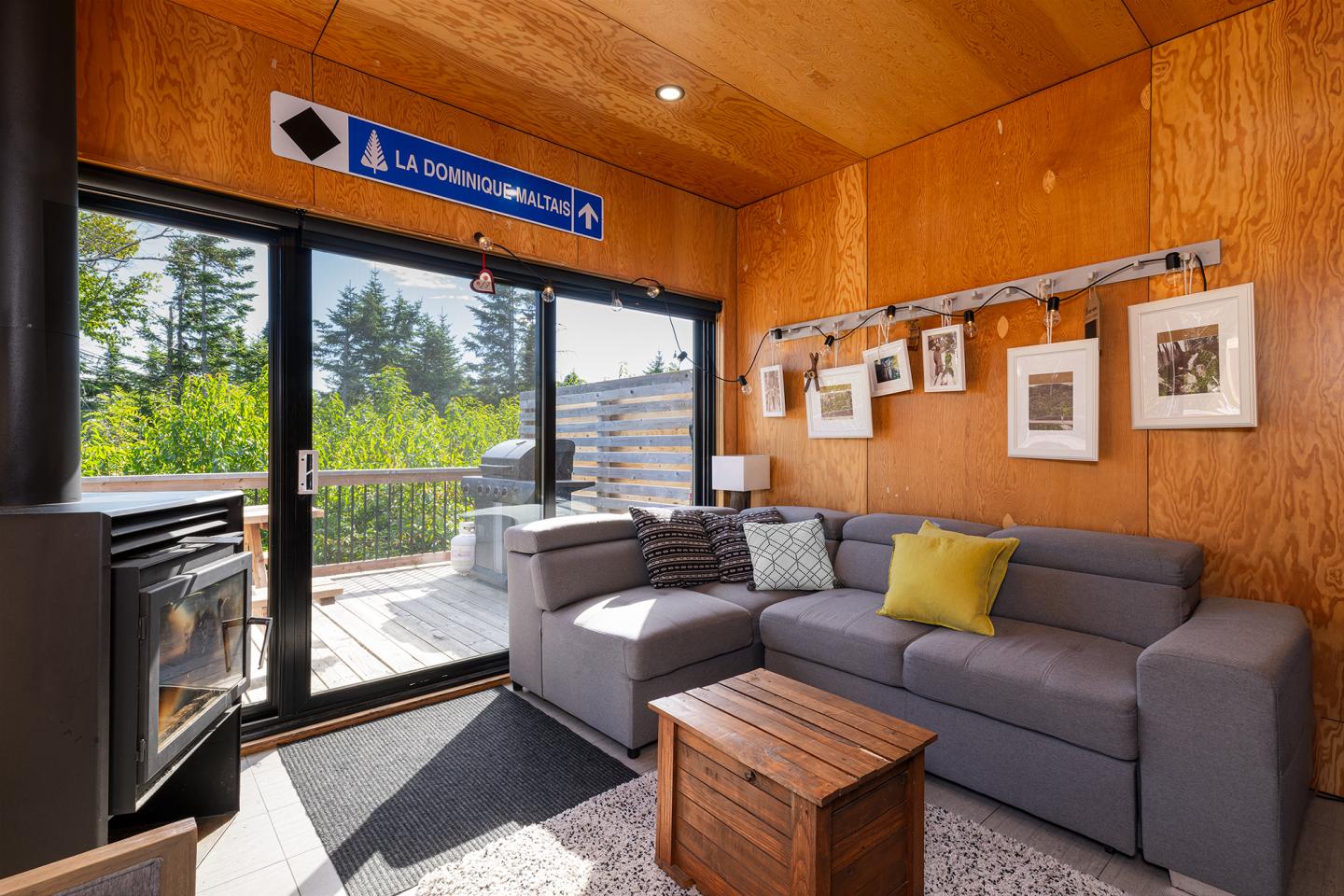 Salon moderne avec canapé gris, poêle à bois, grande fenêtre et tableaux accrochés au mur.