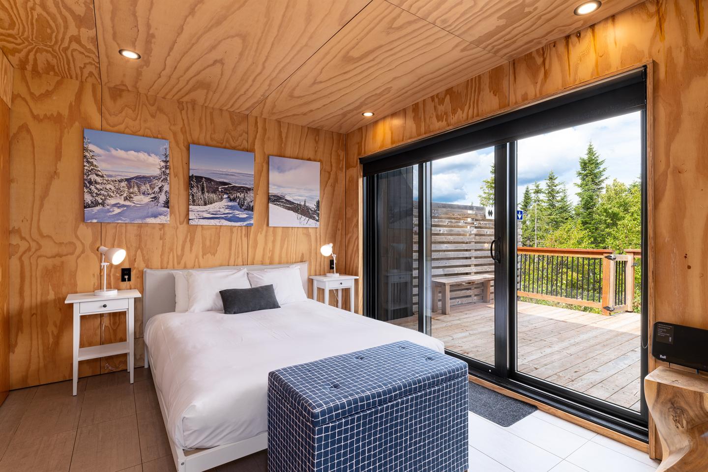 Chambre moderne en bois avec lit, grandes fenêtres et terrasse boisée.