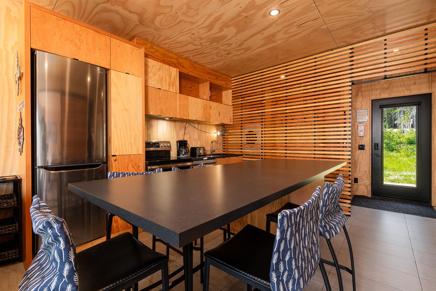 Cuisine moderne avec meubles en bois, table noire et chaises bleues, lumière naturelle.