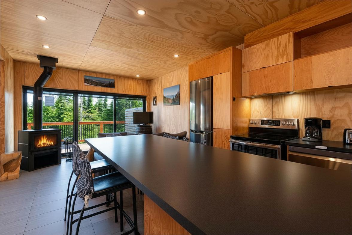 Cuisine moderne en bois avec cheminée, grande table et vue sur jardin verdoyant.