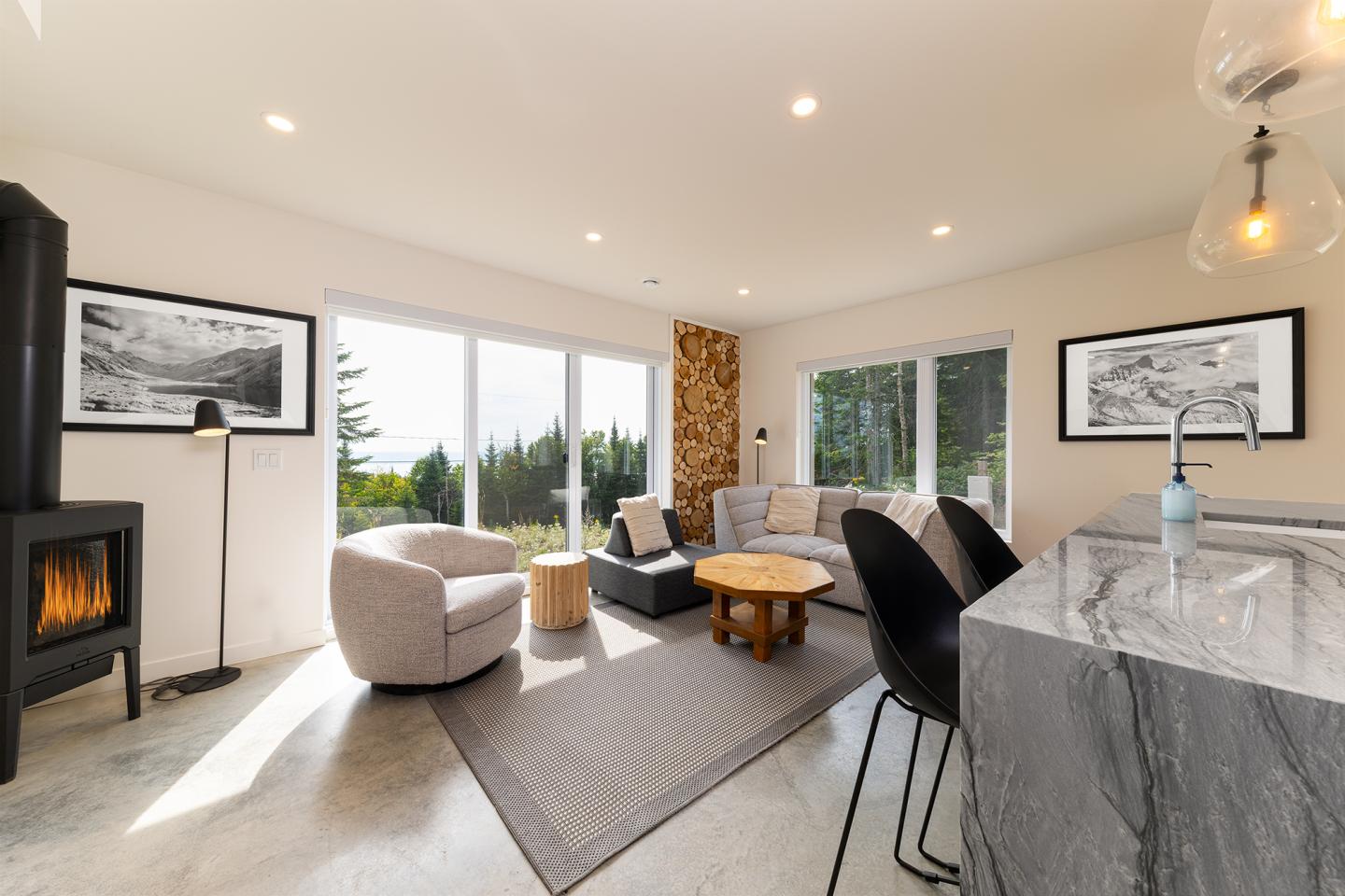 Salon moderne avec canapés gris, cheminée, grandes fenêtres, et îlot central.