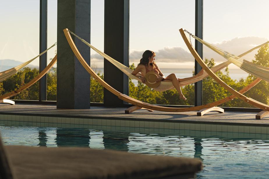Personne relaxant dans un hamac près d'une piscine intérieure au coucher du soleil.