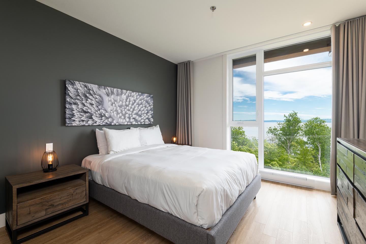 Chambre moderne avec lit double, vue sur mer et forêt par une grande baie vitrée.