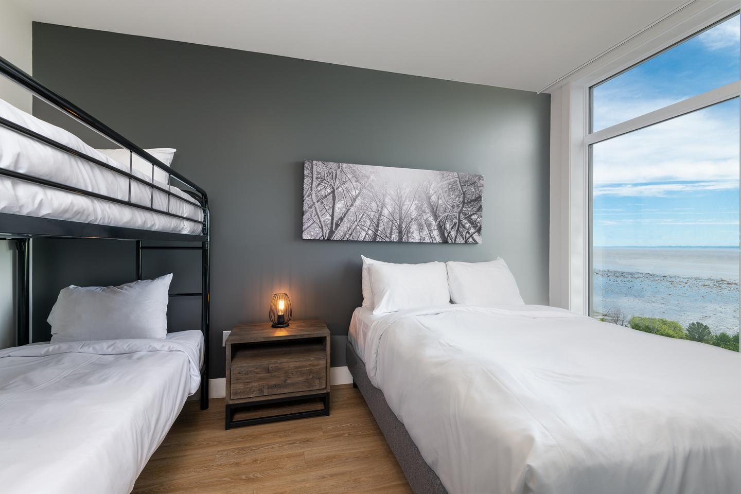 Chambre moderne avec lit double, lits superposés et vue océan.