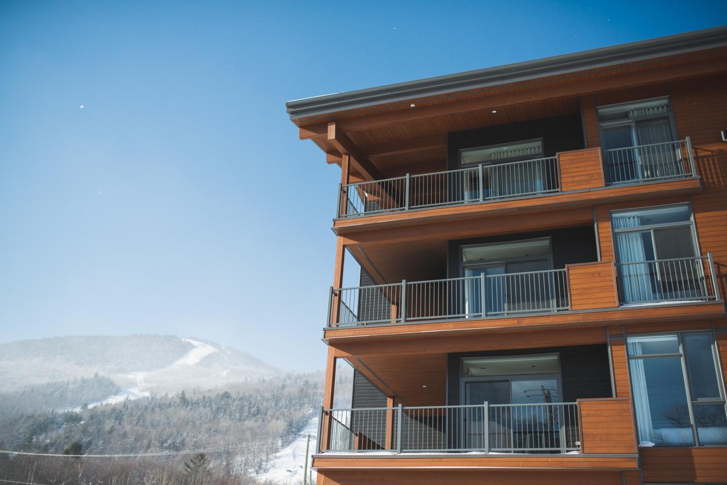 Immeuble moderne en bois avec des balcons, ciel bleu en arrière-plan.