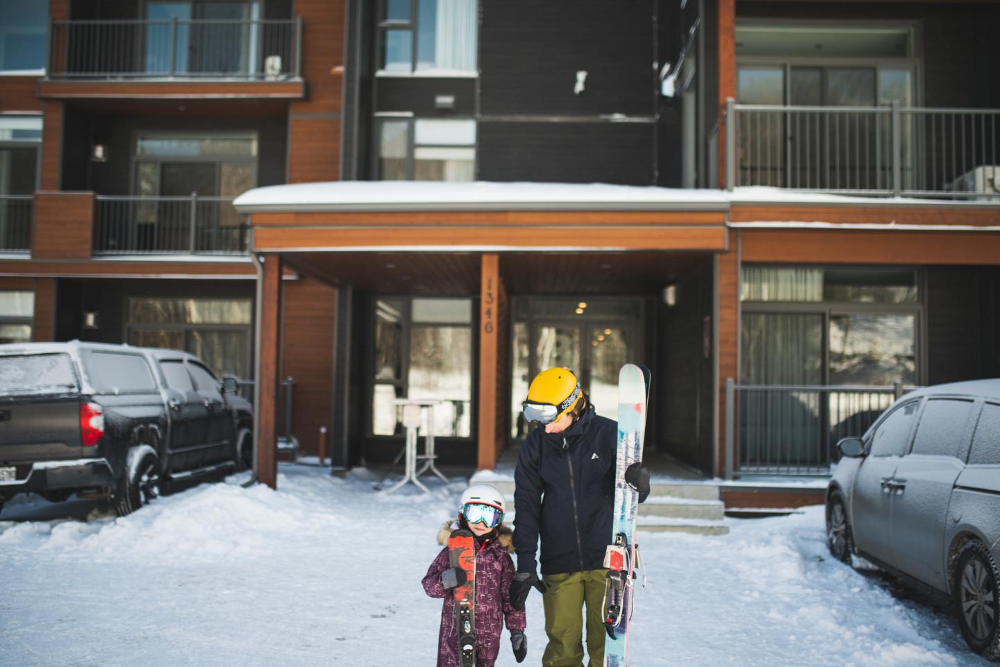 Deux personnes en tenue de ski devant un immeuble enneigé.