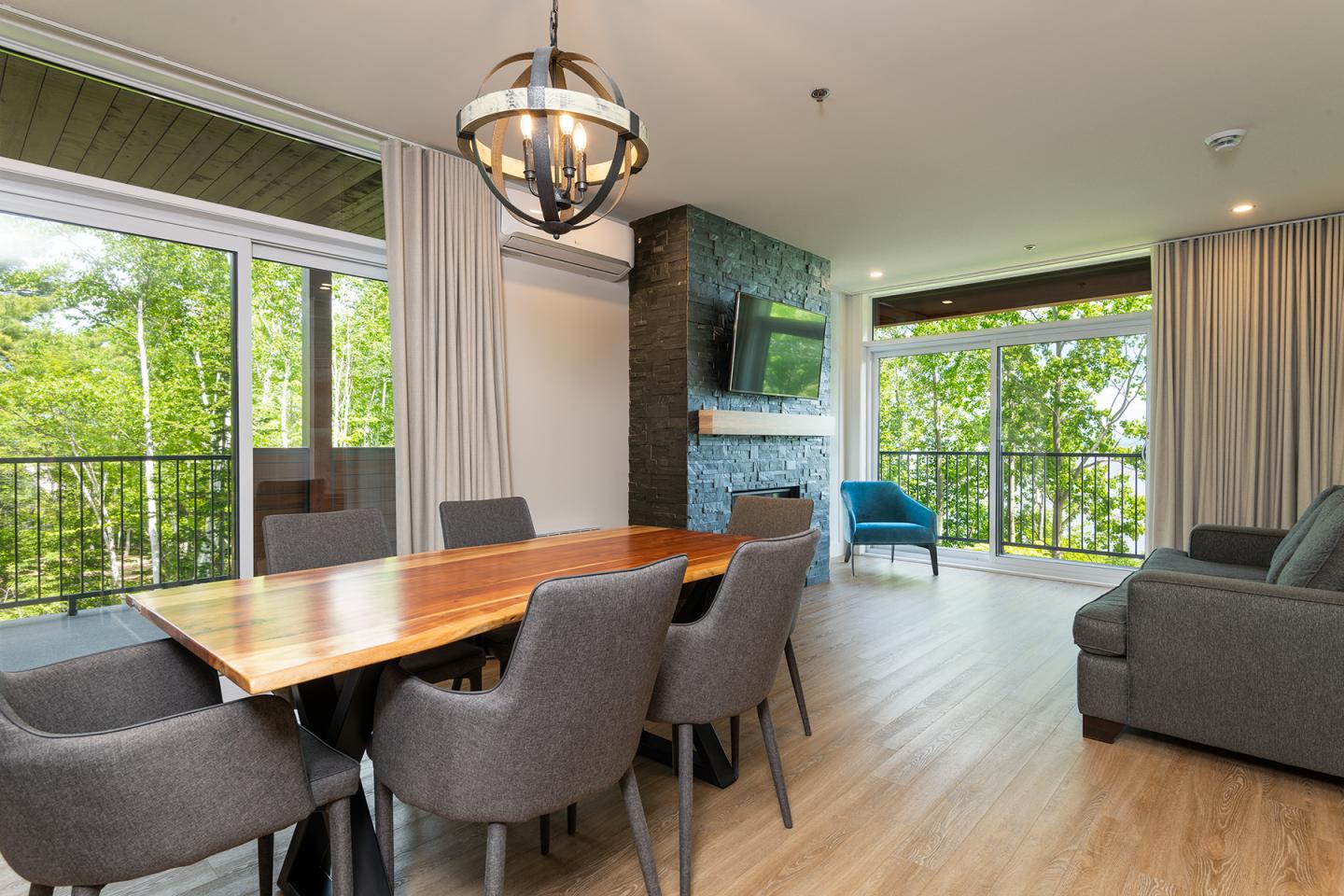 Salle à manger moderne avec table en bois, chaises grises, grand salon et baies vitrées.