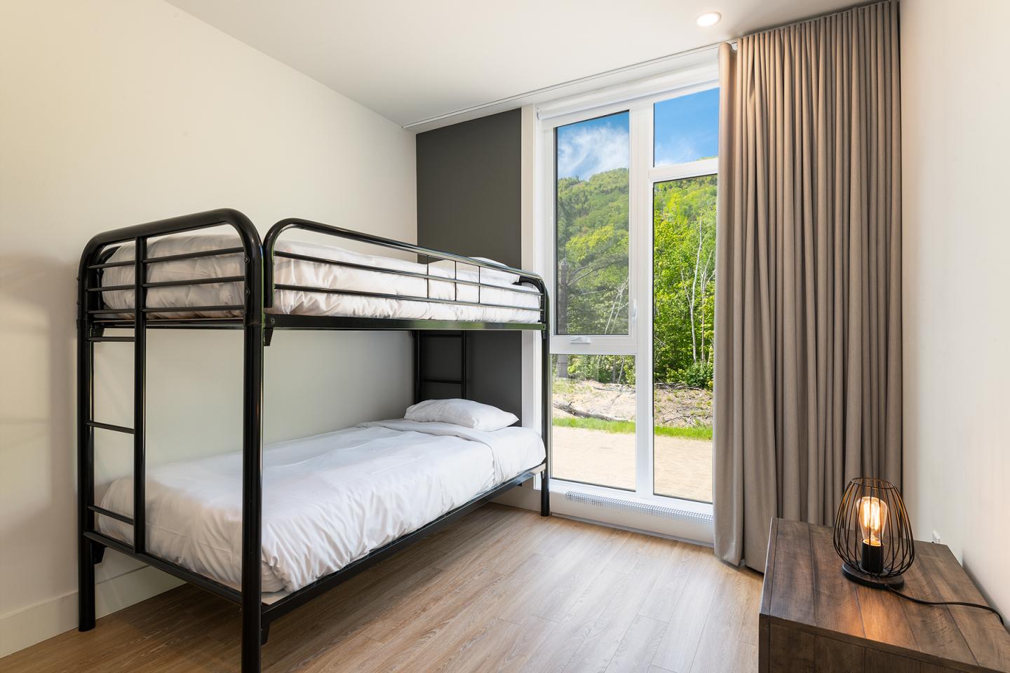 Chambre avec lit superposé, fenêtre lumineuse et table de nuit en bois.