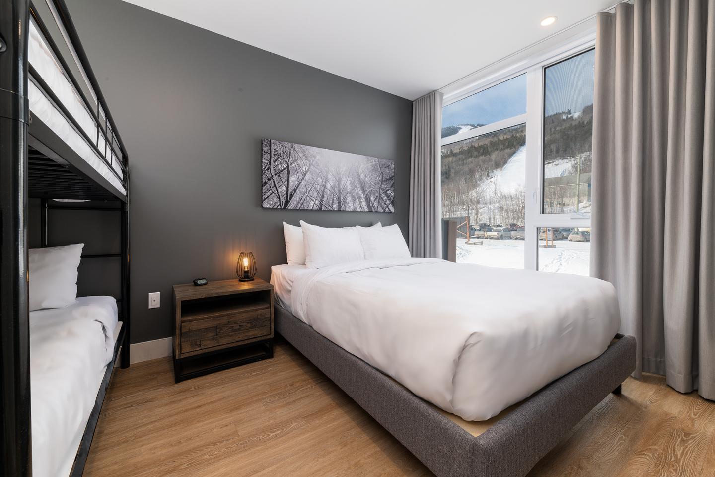 Chambre moderne avec lit double, lits superposés et vue sur montagne enneigée.