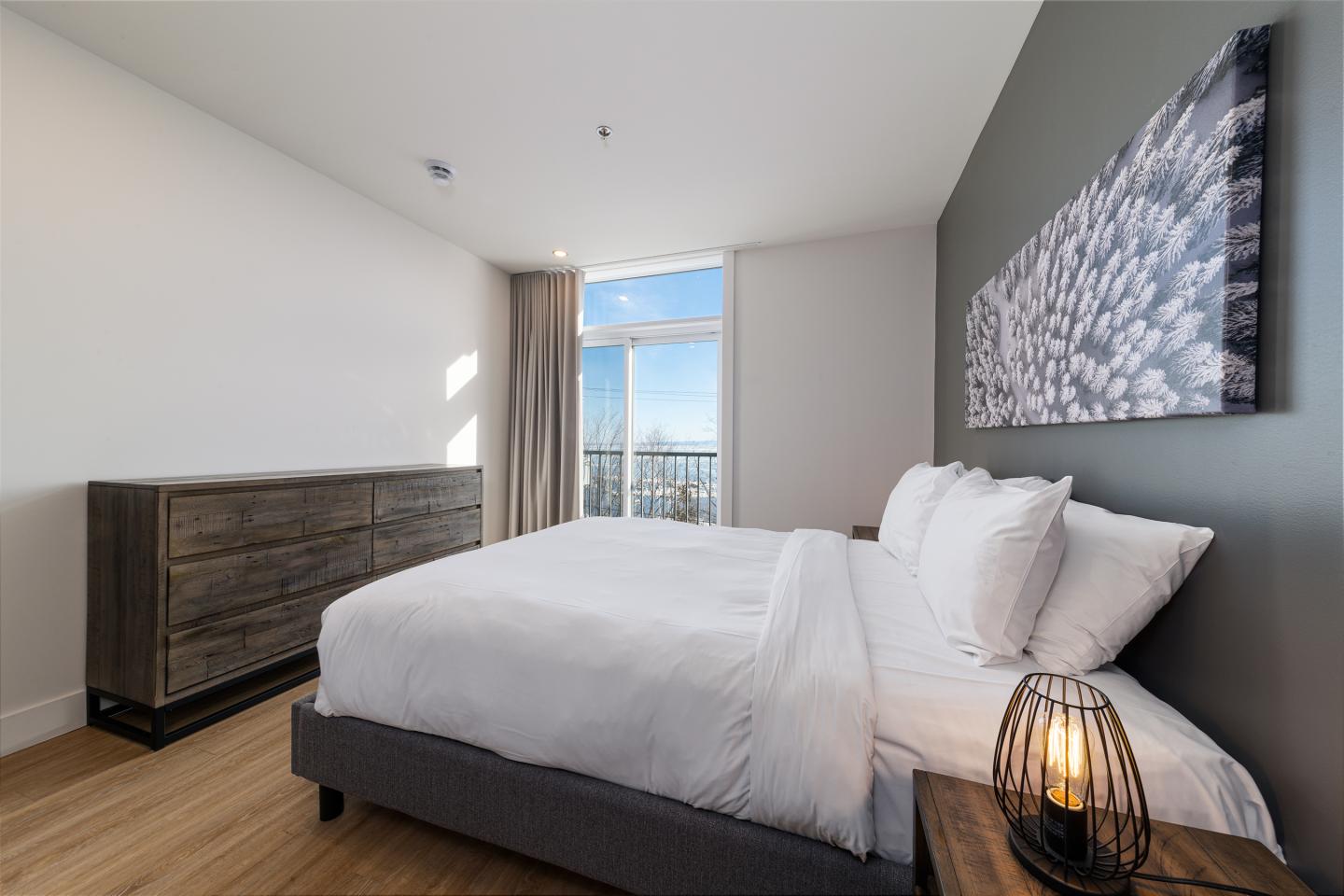 Chambre lumineuse avec lit double, commode en bois et lampe décorative.