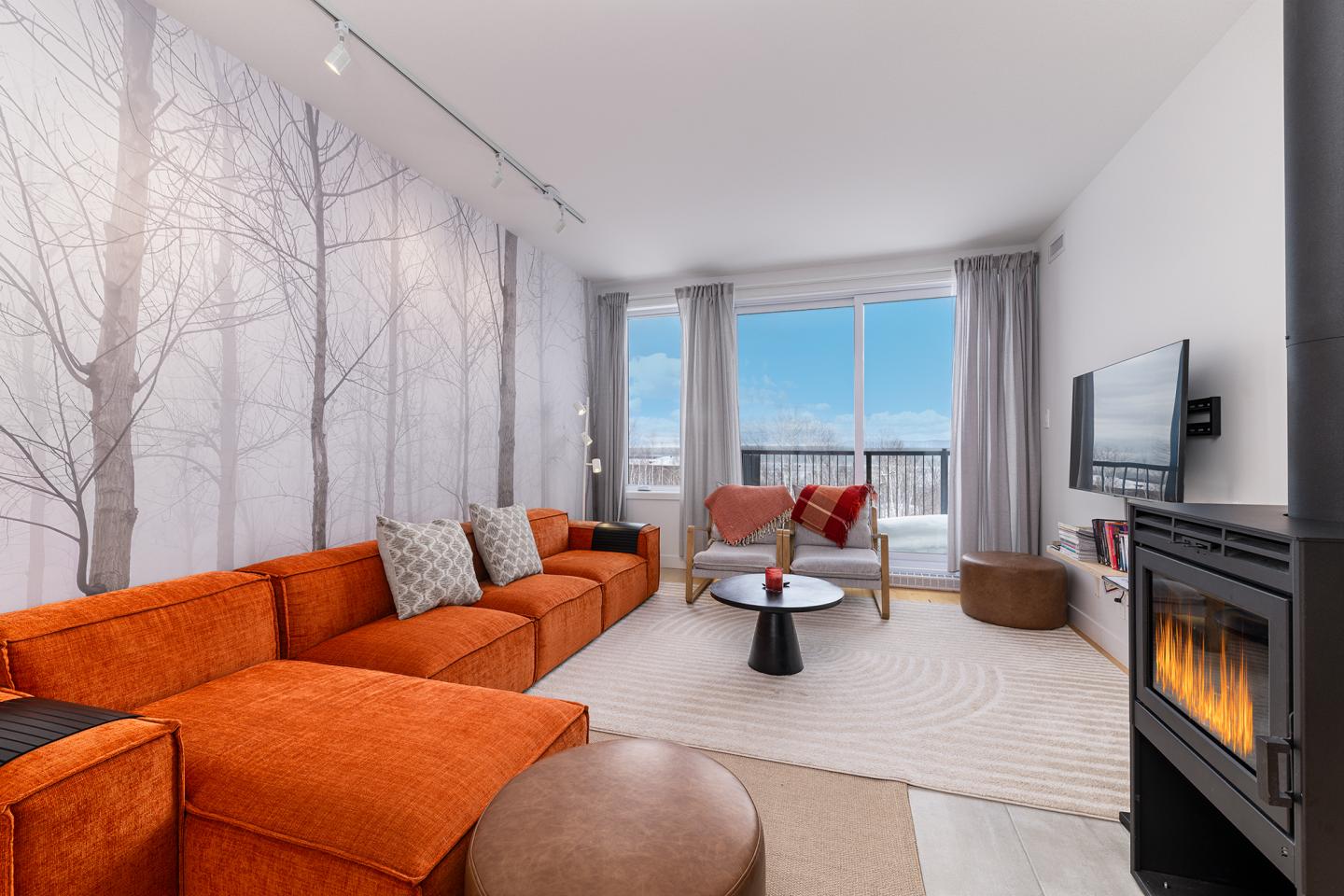 Salon moderne avec canapé orange, poêle à bois, et vue sur balcon enneigé.