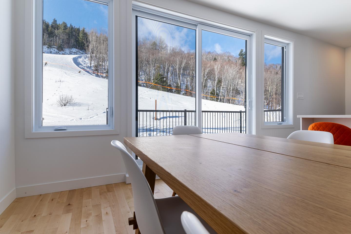 Salle à manger ensoleillée avec vue sur paysage enneigé par grandes fenêtres.