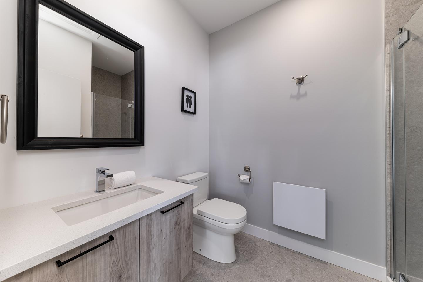 Salle de bain moderne avec lavabo, miroir noir et toilettes.