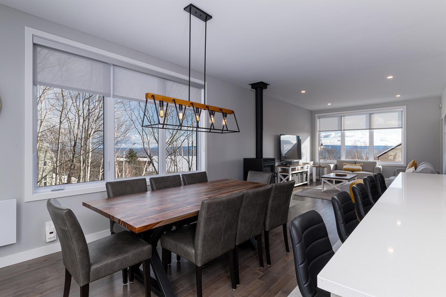 Salle à manger moderne avec table en bois et chaises noires, fenêtres en arrière-plan.