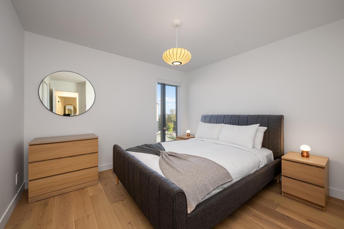Chambre moderne avec lit double, miroir rond et commodes en bois.