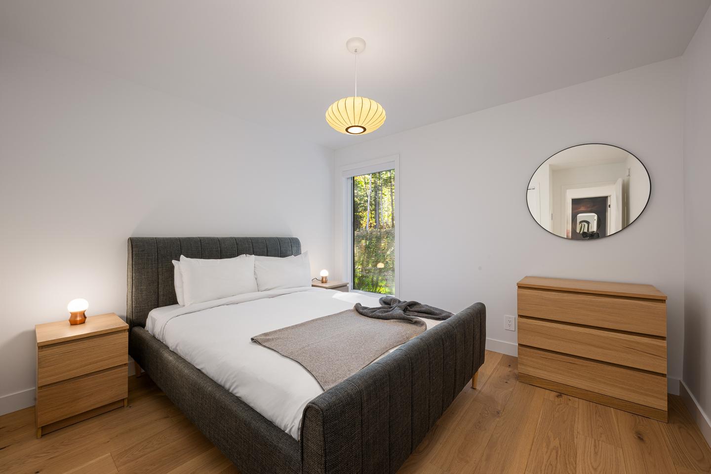 Chambre moderne avec lit, tables de chevet et miroir rond.