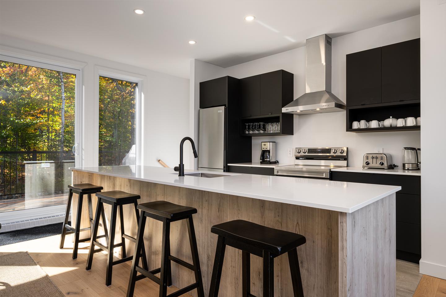 Cuisine moderne avec îlot en bois, tabourets noirs, et appareils en acier inoxydable.