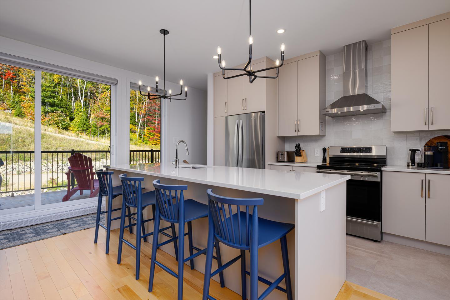 Cuisine moderne avec îlot central, chaises bleues et vue sur jardin.