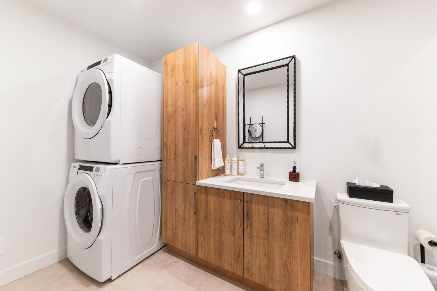 Salle de bain moderne avec machine à laver, sèche-linge et lavabo en bois clair.