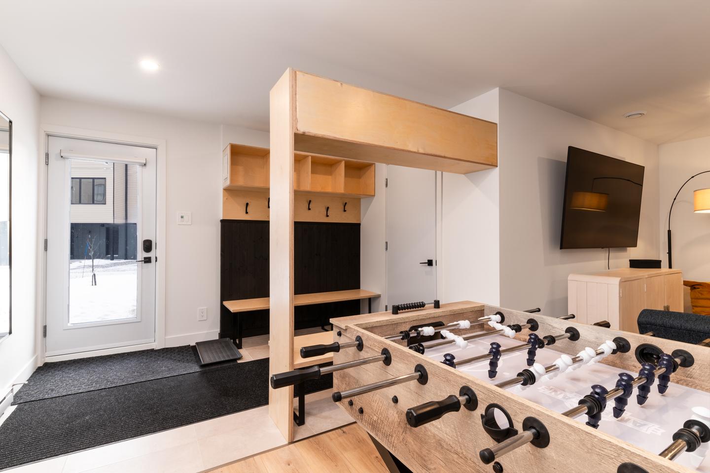 Salle de jeu moderne avec babyfoot, télé et étagères en bois clair.
