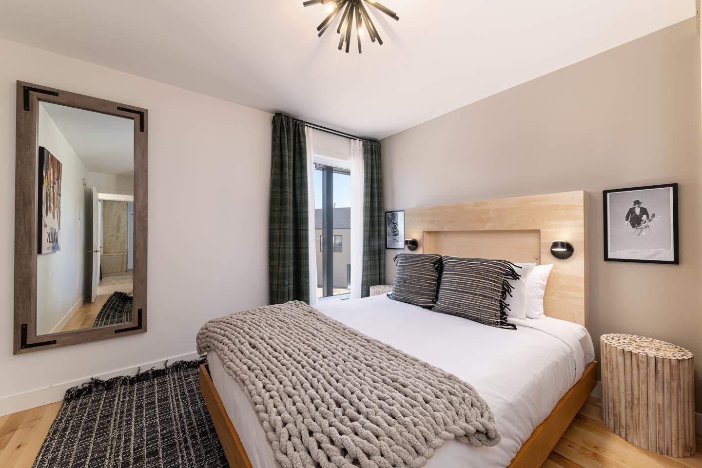 Chambre moderne avec lit double, miroir, et fenêtre à rideaux verts.