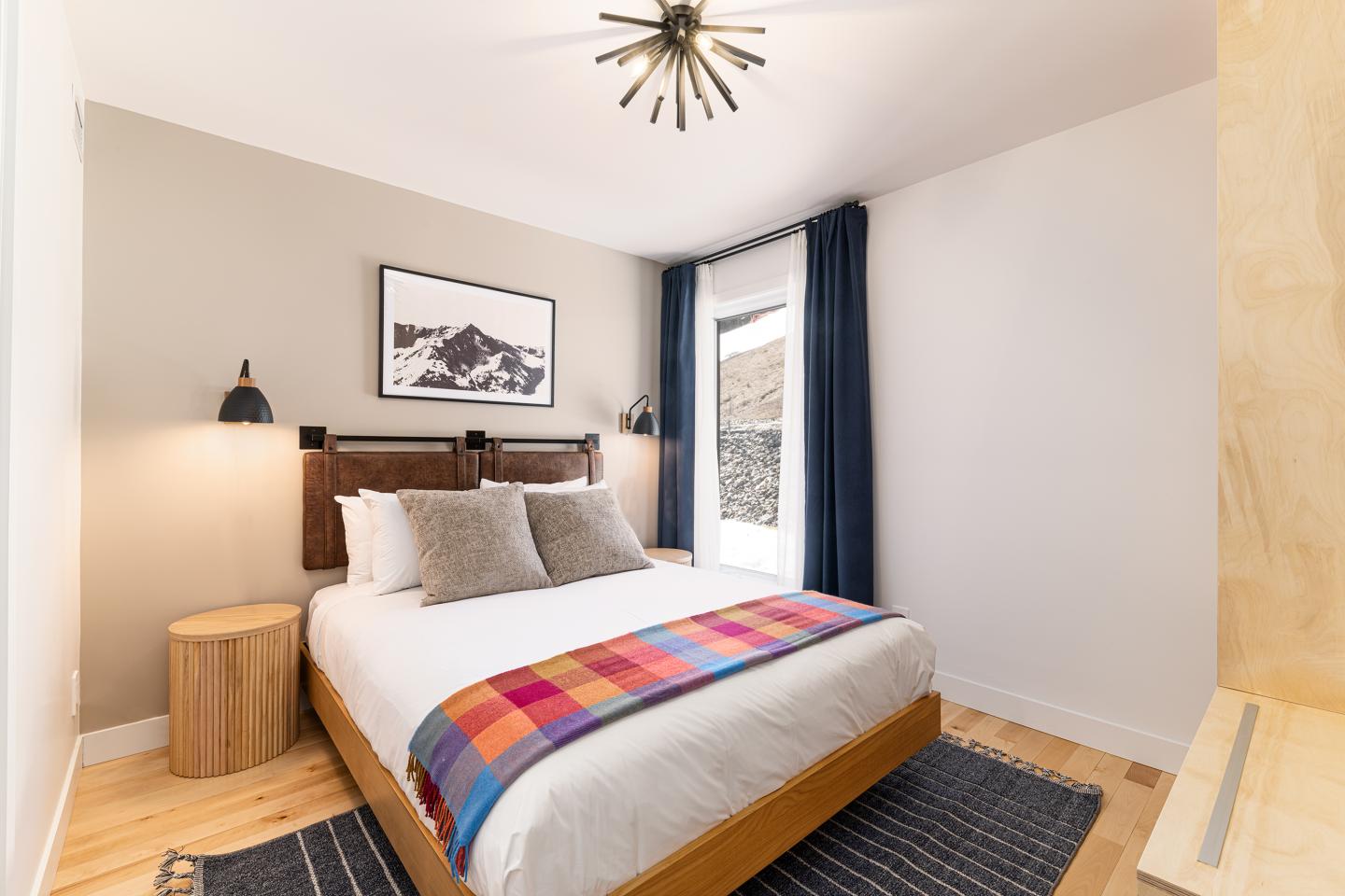 Chambre lumineuse avec lit double, plaid coloré, et décoration moderne.
