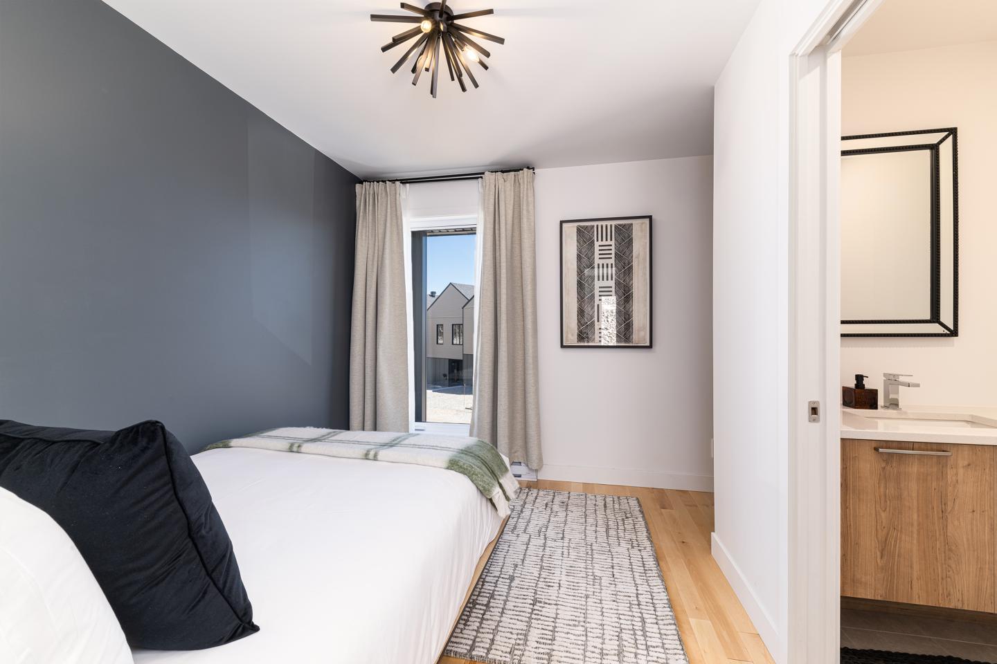 Chambre moderne avec mur bleu-gris, lit blanc, salle de bain attenante.