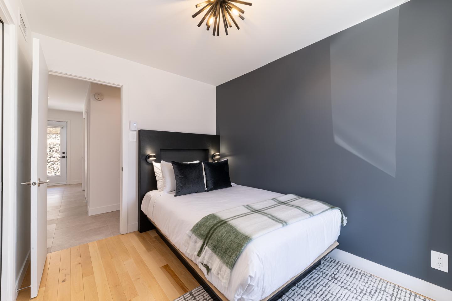 Chambre moderne avec mur gris, lit double et plaid vert. Luminaire design au plafond.
